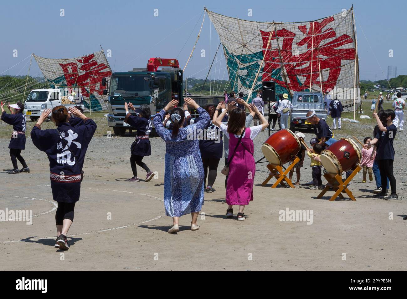 Sagamihara, Japan, May 5th. 2023, Festival supporters dance in front of large kites on display at the Sagami Giant Kite festival (Sagami-no-Oodako) Sagamihara. The Sagami Giant Kite festival began in the 1830s as an addition to the Children's Festival which is celebrated in japan on May 5th. Over time the kites, which are made of bamboo and handmade paper, have got bigger. The largest kites flown from the Sagami riverside during this festival measure around 15 metres on their longest side and can weigh over 900 kilograms. It takes a team of between 80 and 100 people to launch them into air. Stock Photo