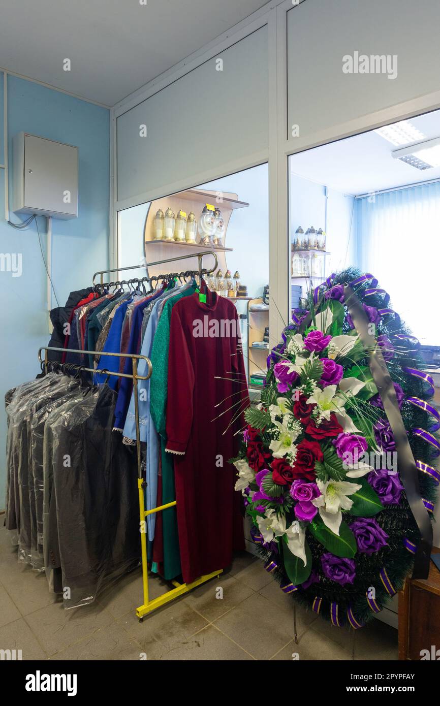 Hangers with men suits and women clothes for the deceased in a funeral goods store. The clothes in which the deceased is escorted to the last journey. Stock Photo