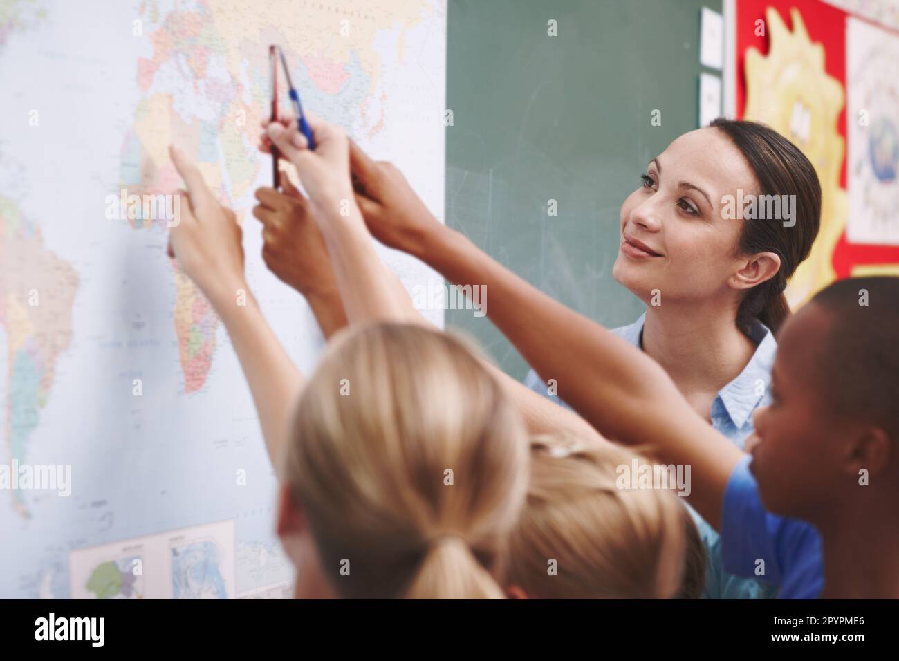 Showing them around a world map. An excited class pointing at a world map with their geography teacher. Stock Photo
