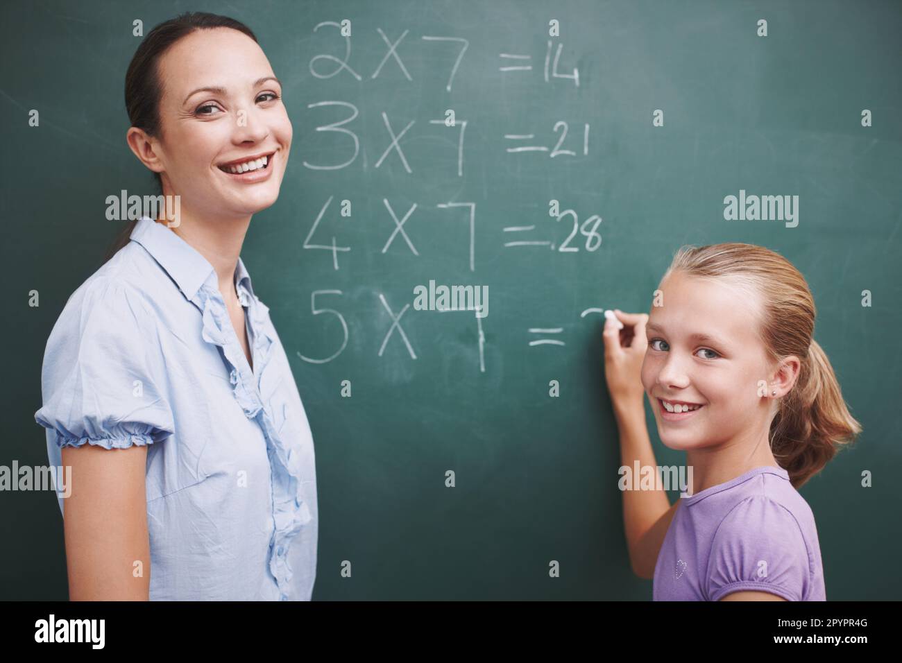 Helping her with her sums. A pretty teacher standing at the blackboard ...