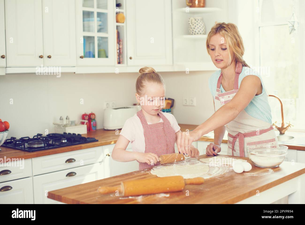 Adding a sprinkle of flour. Cute little girl baking in the kitchen with ...