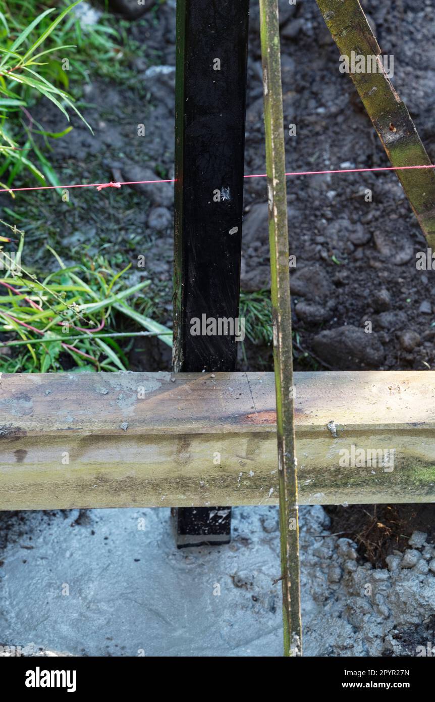 Timber is used to support a black steel fence post while the concrete