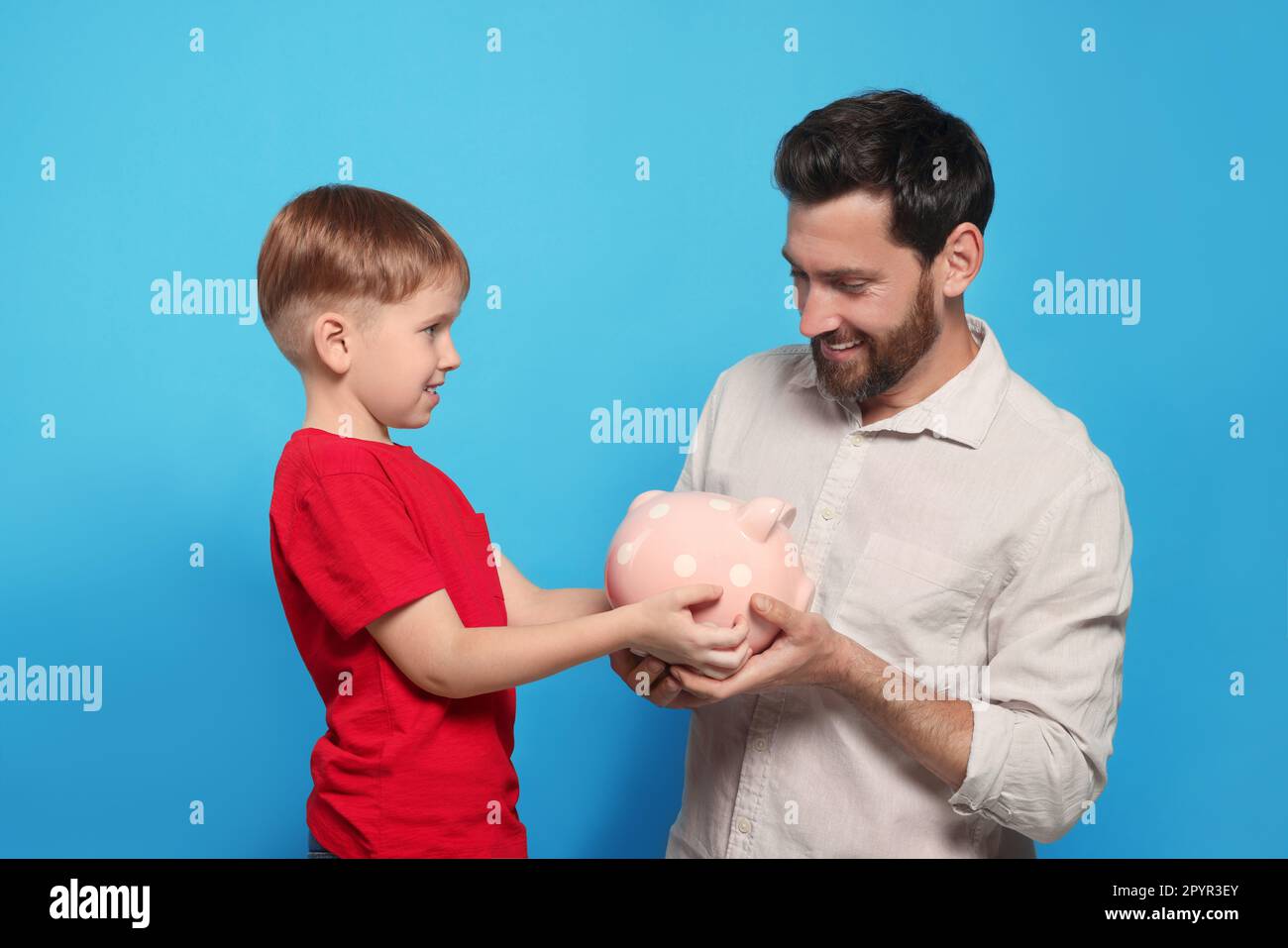 Father and his son with ceramic piggy bank on light blue background ...