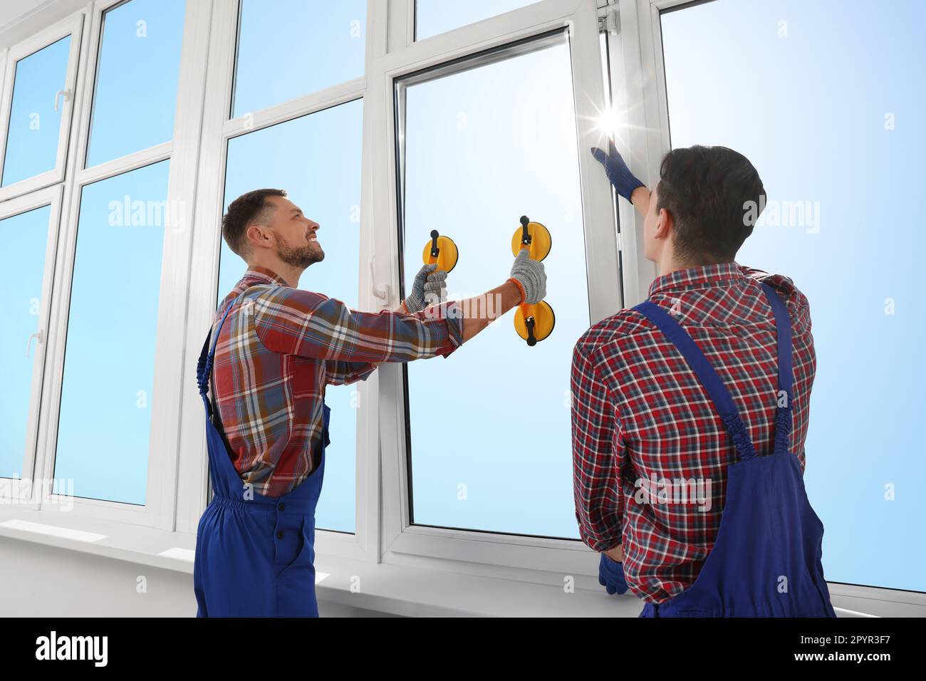 Workers using suction lifters during plastic window installation indoors Stock Photo