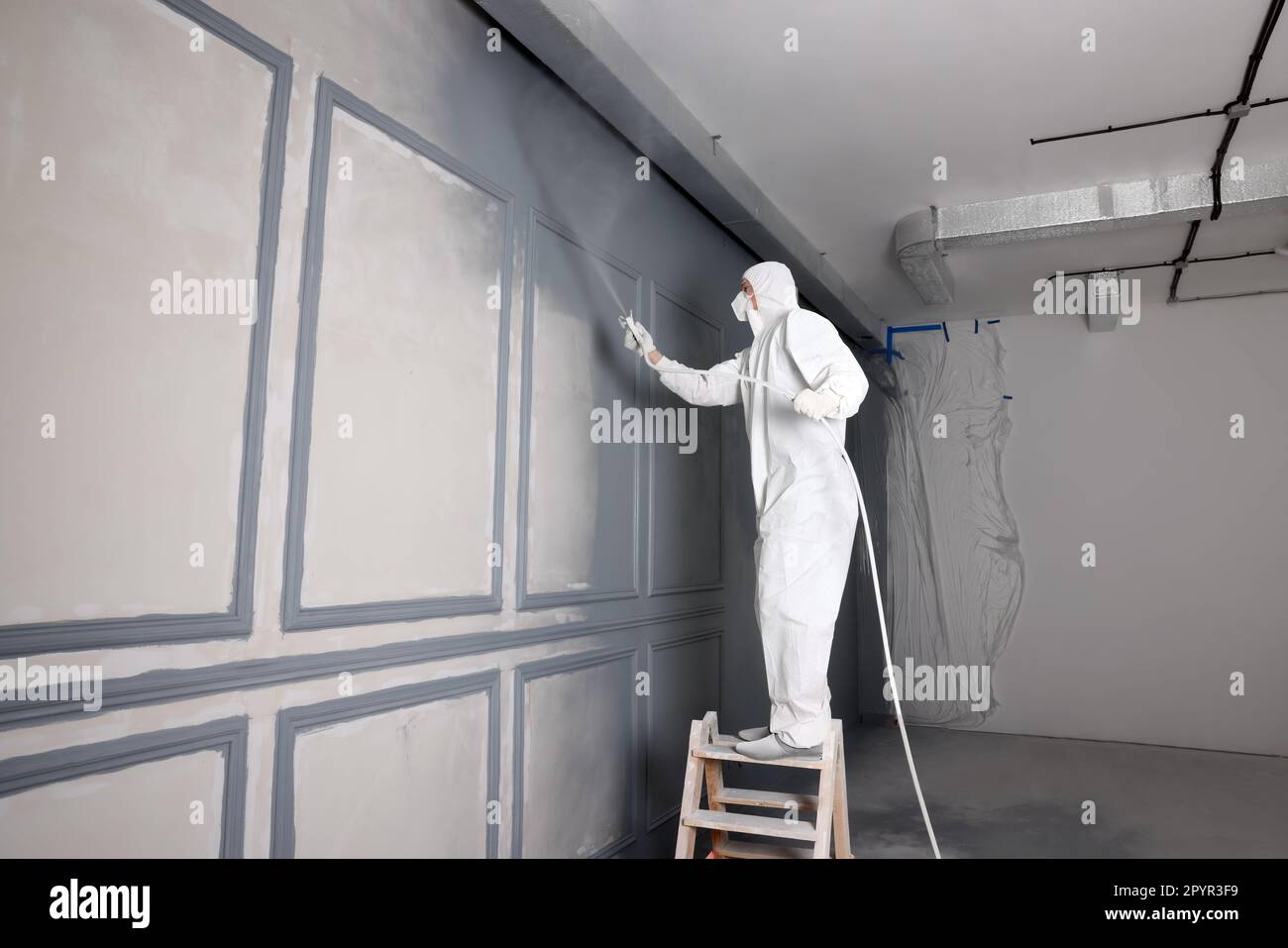 Decorator dyeing wall in grey color with spray paint indoors Stock
