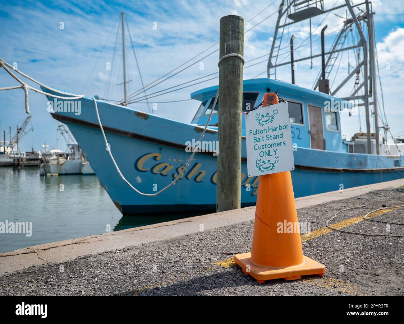 FULTON, TX - 14 FEB 2023: Parking Sign on an orange traffic warning cone, near a blue commercial fishing boat, moored by ropes to a wood piling in the Stock Photo