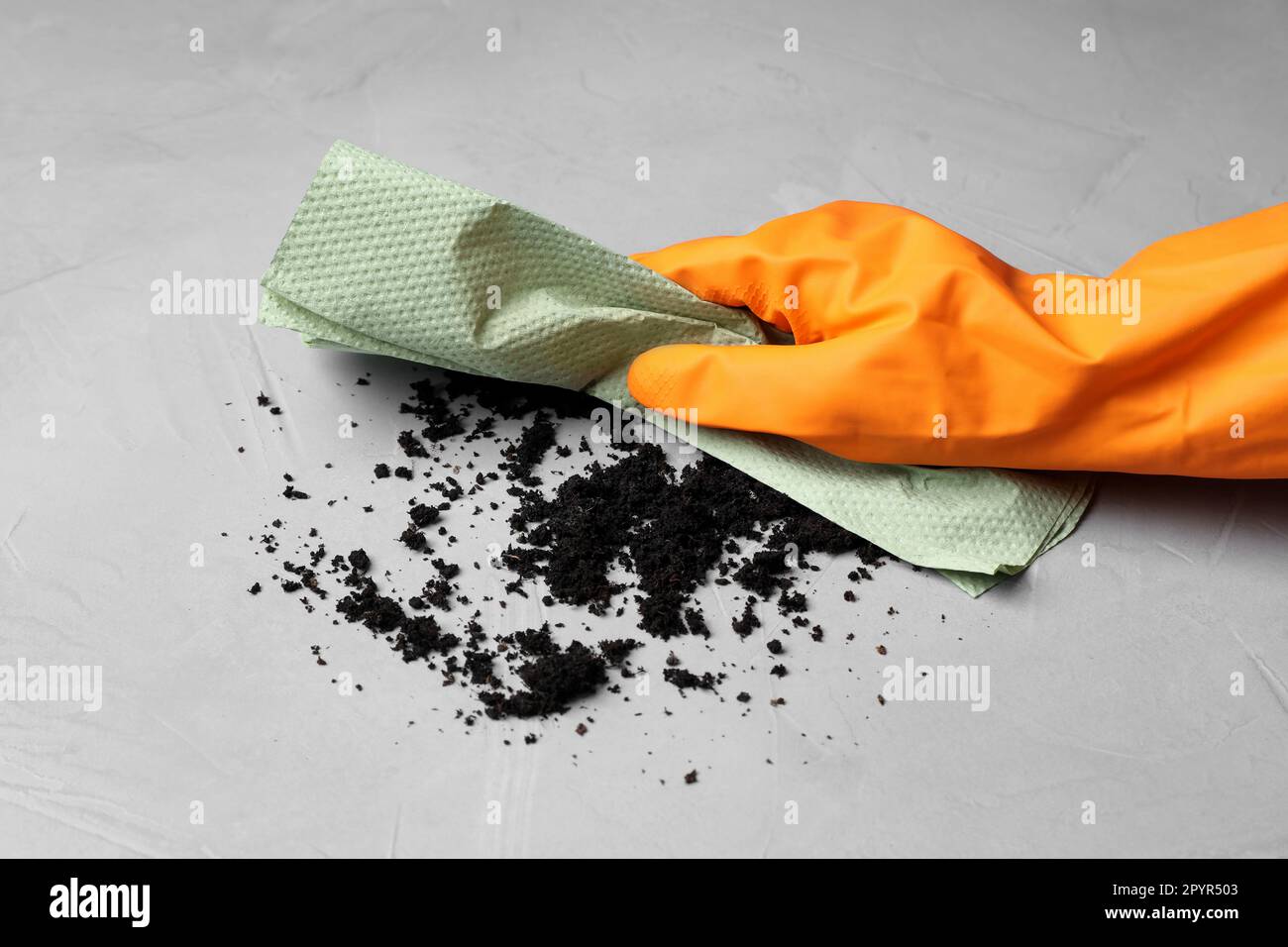 Woman in glove sweeping scattered coffee grounds with paper towel from