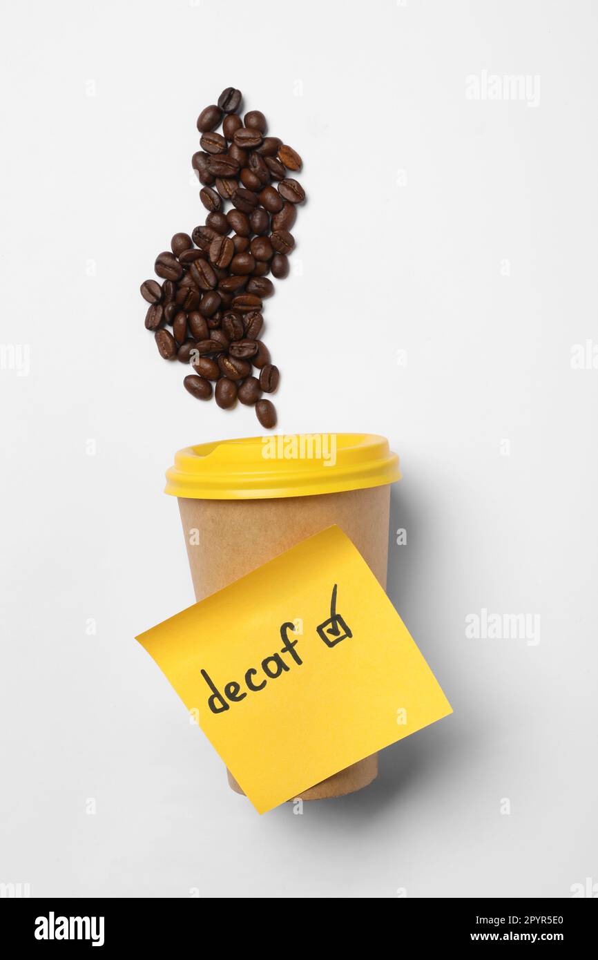 Note with word Decaf attached to takeaway cup and coffee beans on white background, flat lay Stock Photo
