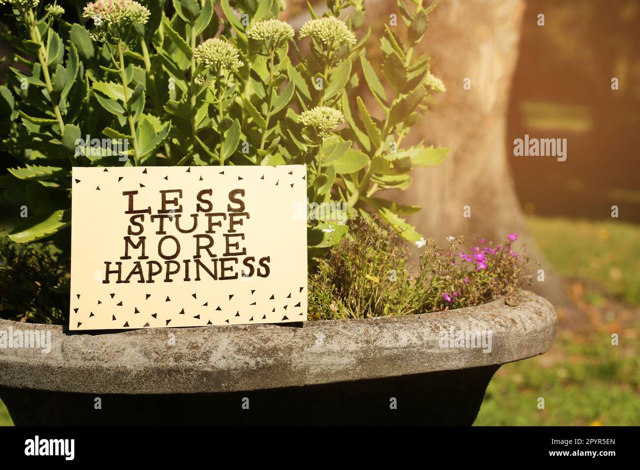 Card with phrase Less Stuff More Happiness on stone planter outdoors, space for text Stock Photo