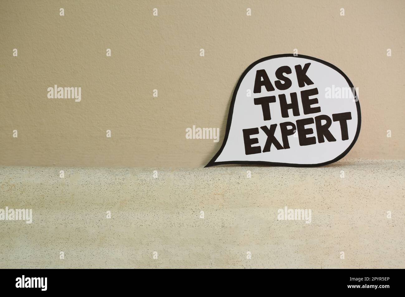Paper message bubble with phrase Ask The Expert near beige wall, space for text Stock Photo