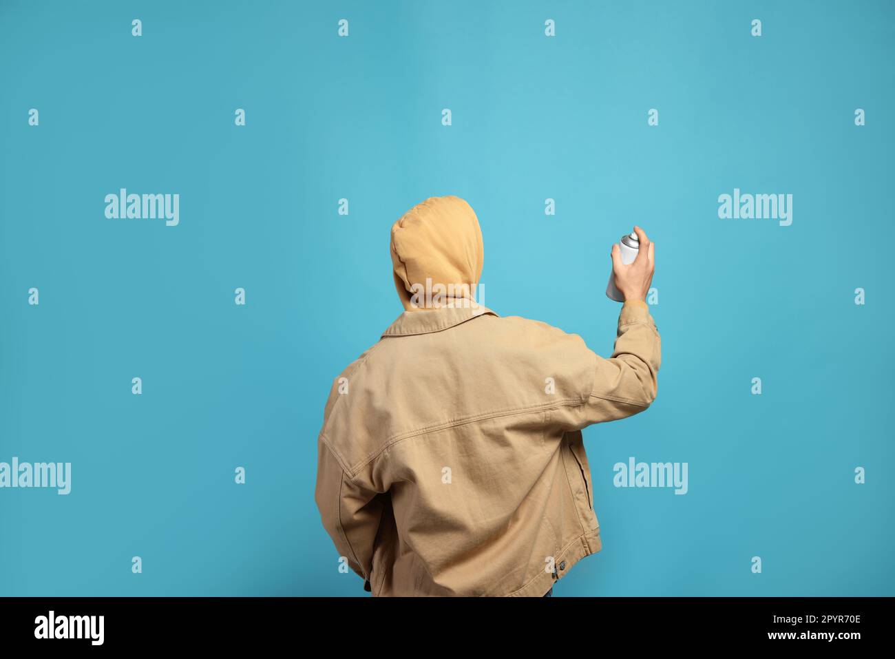 Man holding white can of spray paint on light blue background, back ...