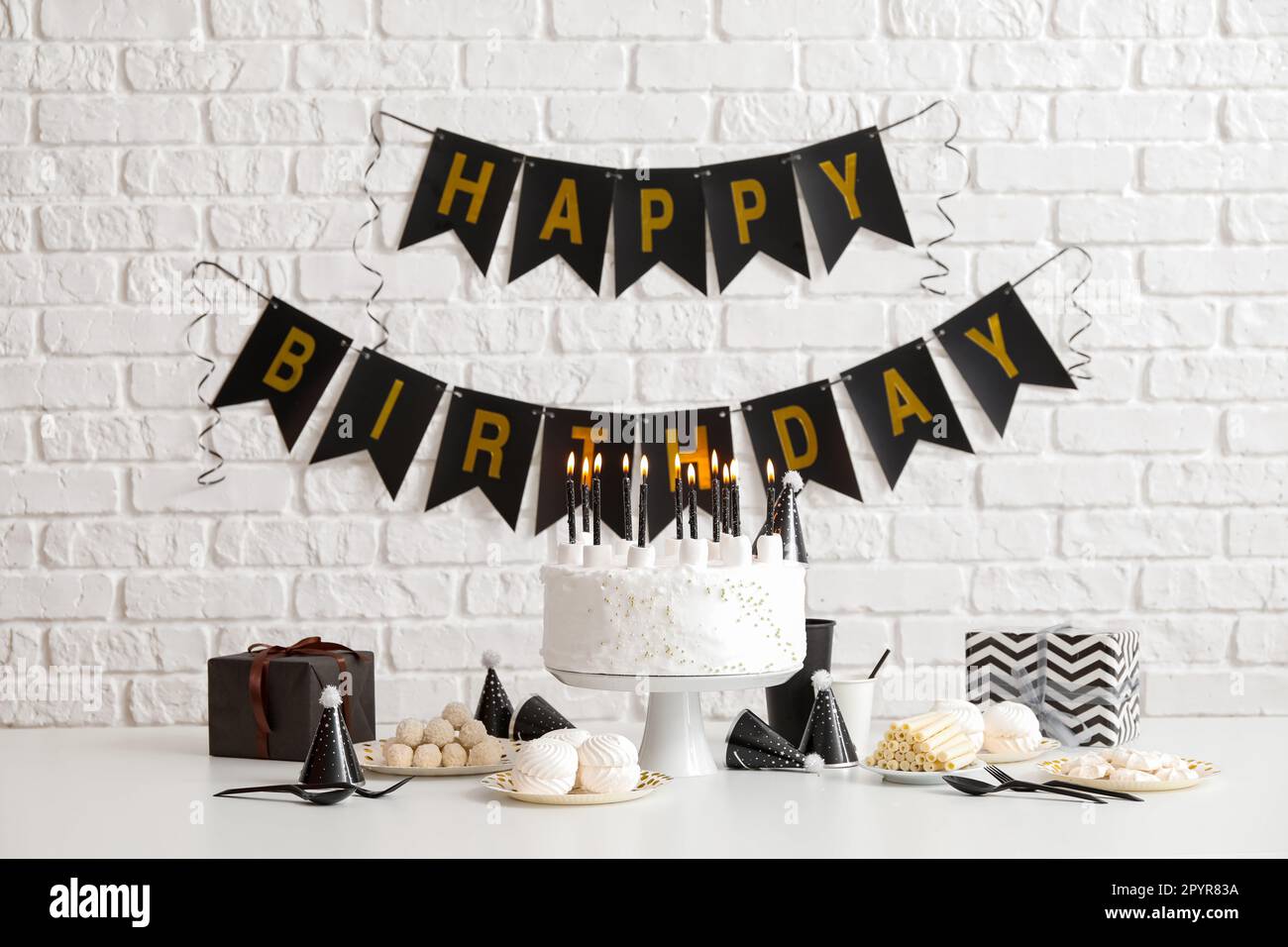 Birthday cake with candles on white table and garlands on brick wall ...