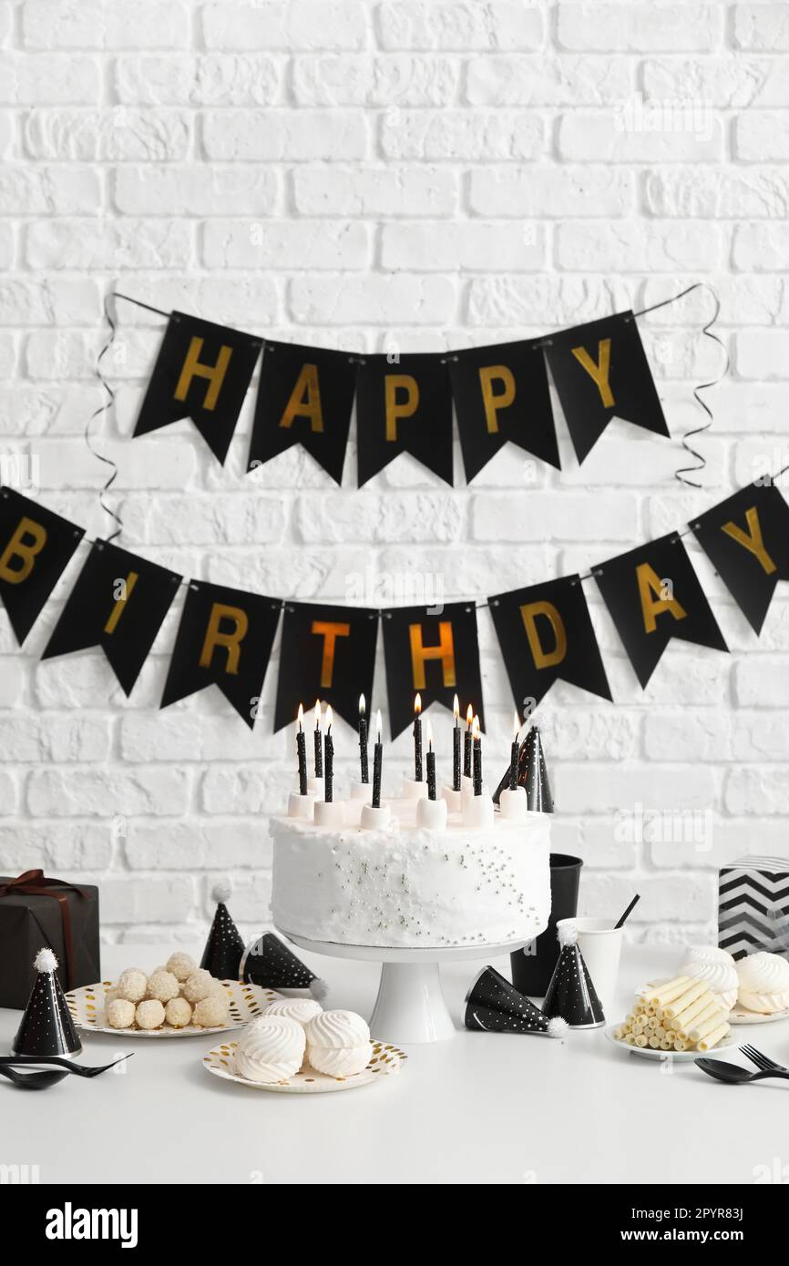 Birthday cake with candles on white table and garlands on brick wall ...