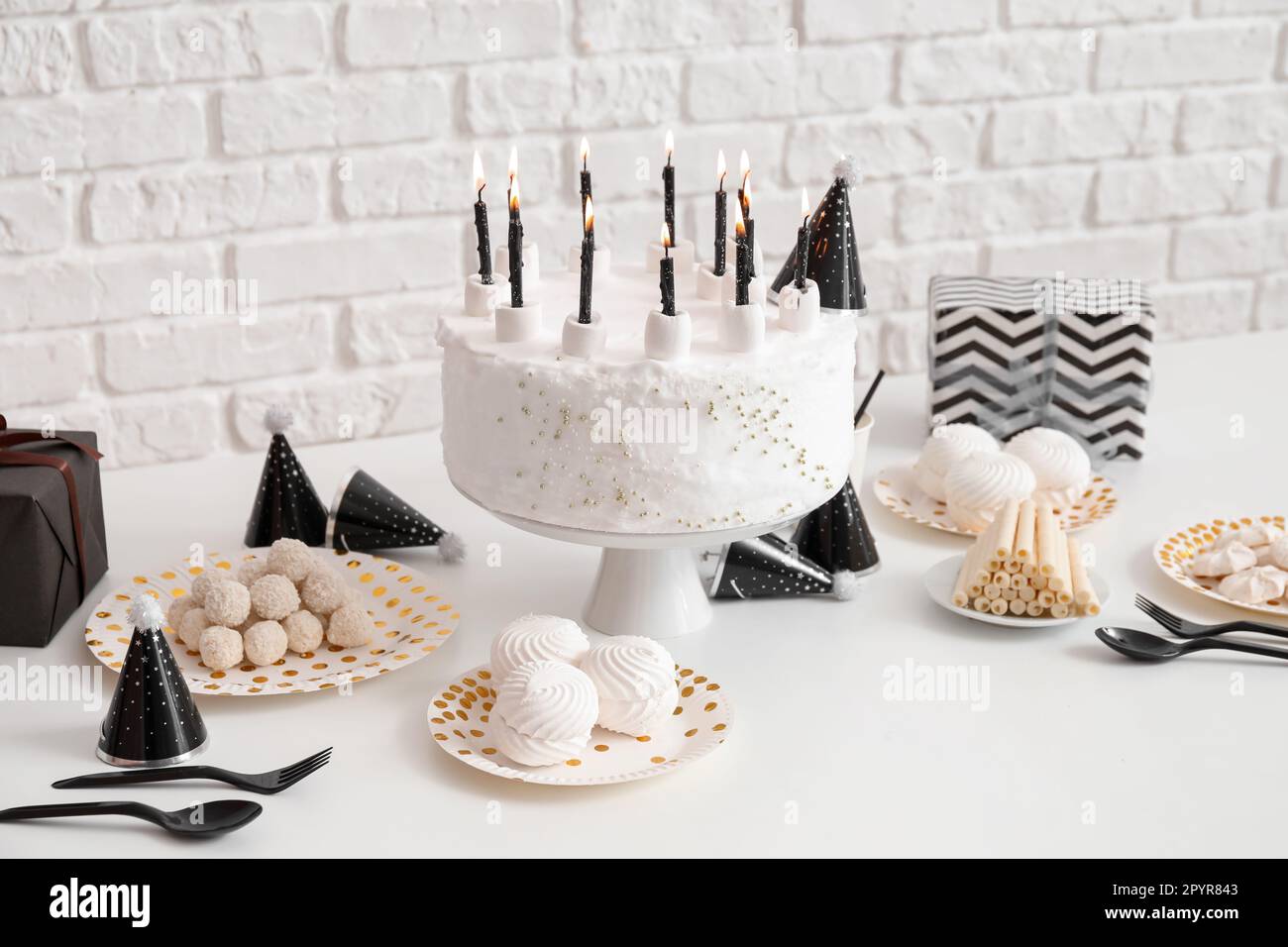 Birthday cake with candles and sweets on white table near brick wall ...