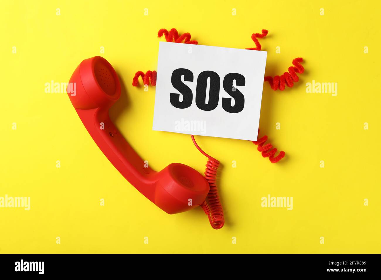 Telephone handset and paper note with abbreviation SOS on yellow
