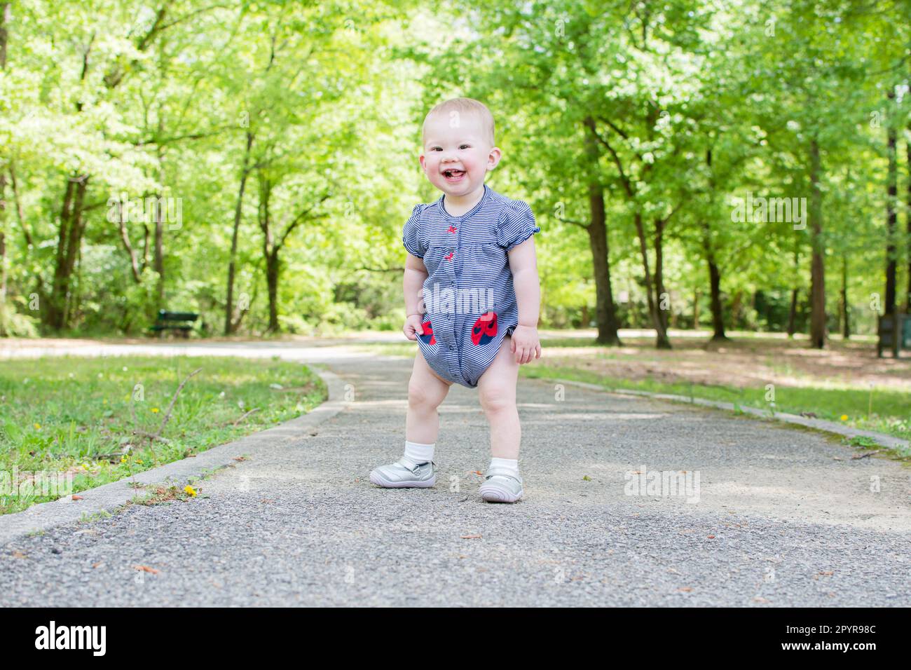 A Toddler is taking her first steps in the park. Baby is learning how to walk. Baby development 1-year-old girl Stock Photo