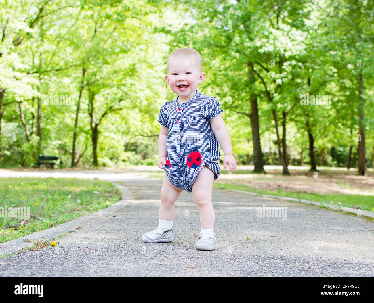 A Toddler is taking her first steps in the park. Baby is learning how to walk. Baby development 1-year-old girl Stock Photo