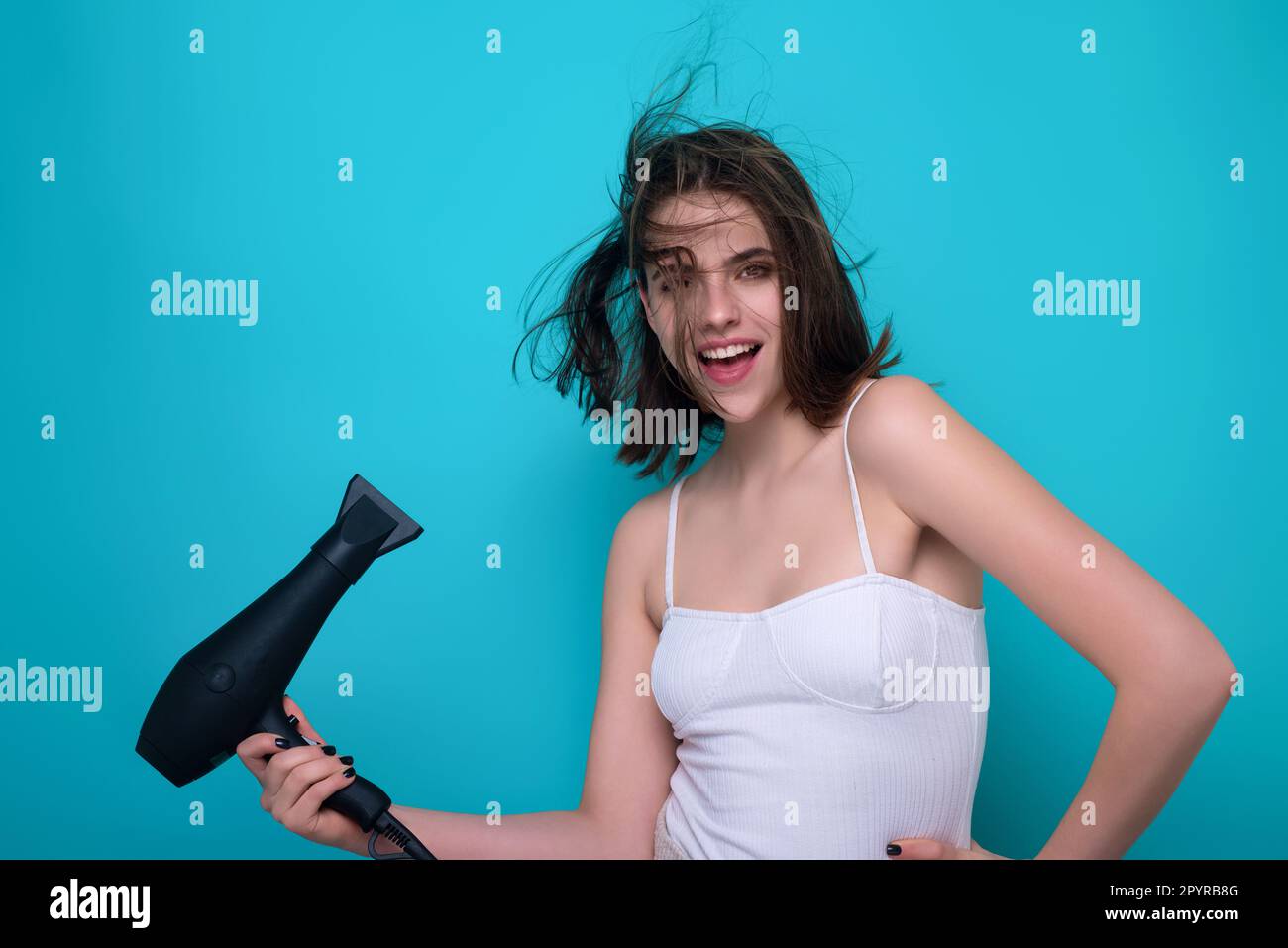 Young woman drying her hair with a hairdryer isolated on studio ...