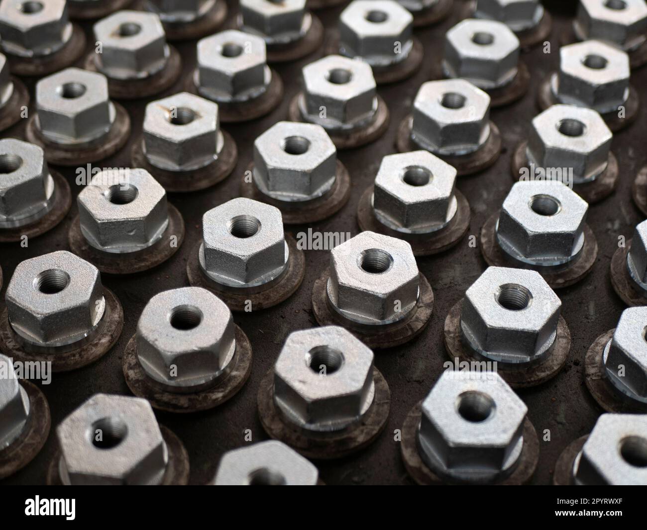 Metal hex bolts in the production, top view and selective focus. Fasteners manufacturing, industrial concept Stock Photo