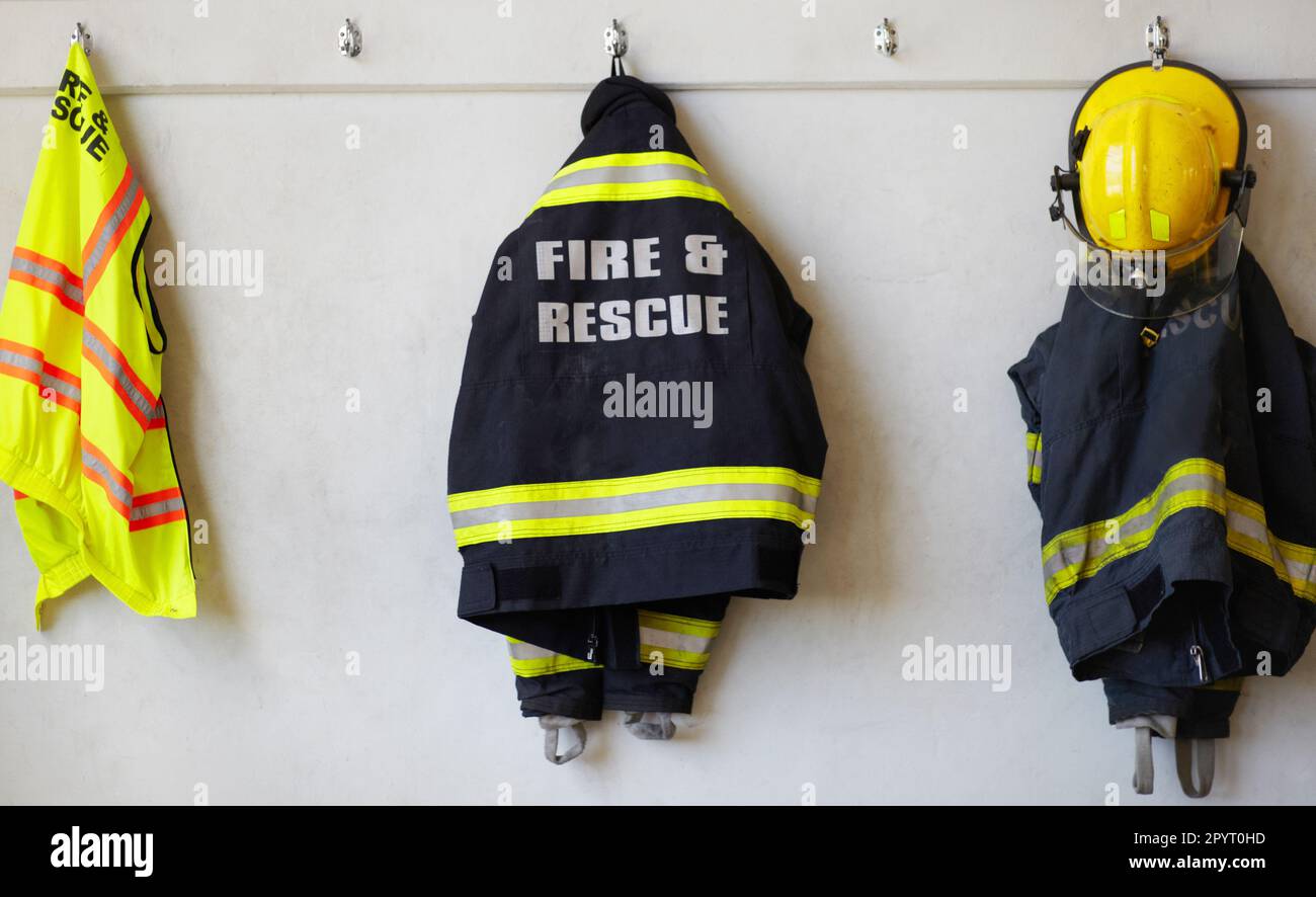 Fireman, uniform and clothing hanging on wall rack at station for fire fighting protection