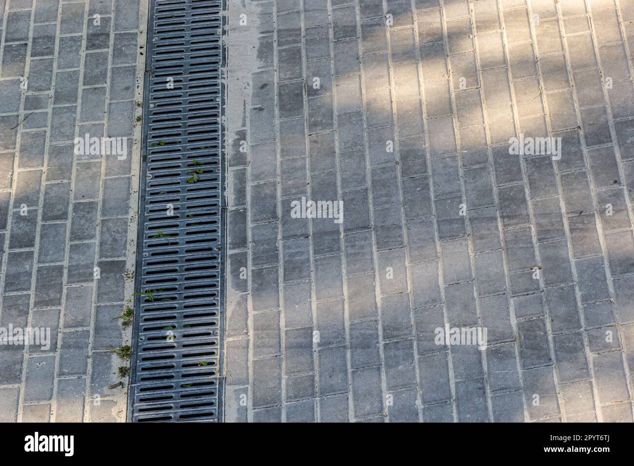 A lattice of a drainage paving system on a footpath made of square stone tiles, close up of a
