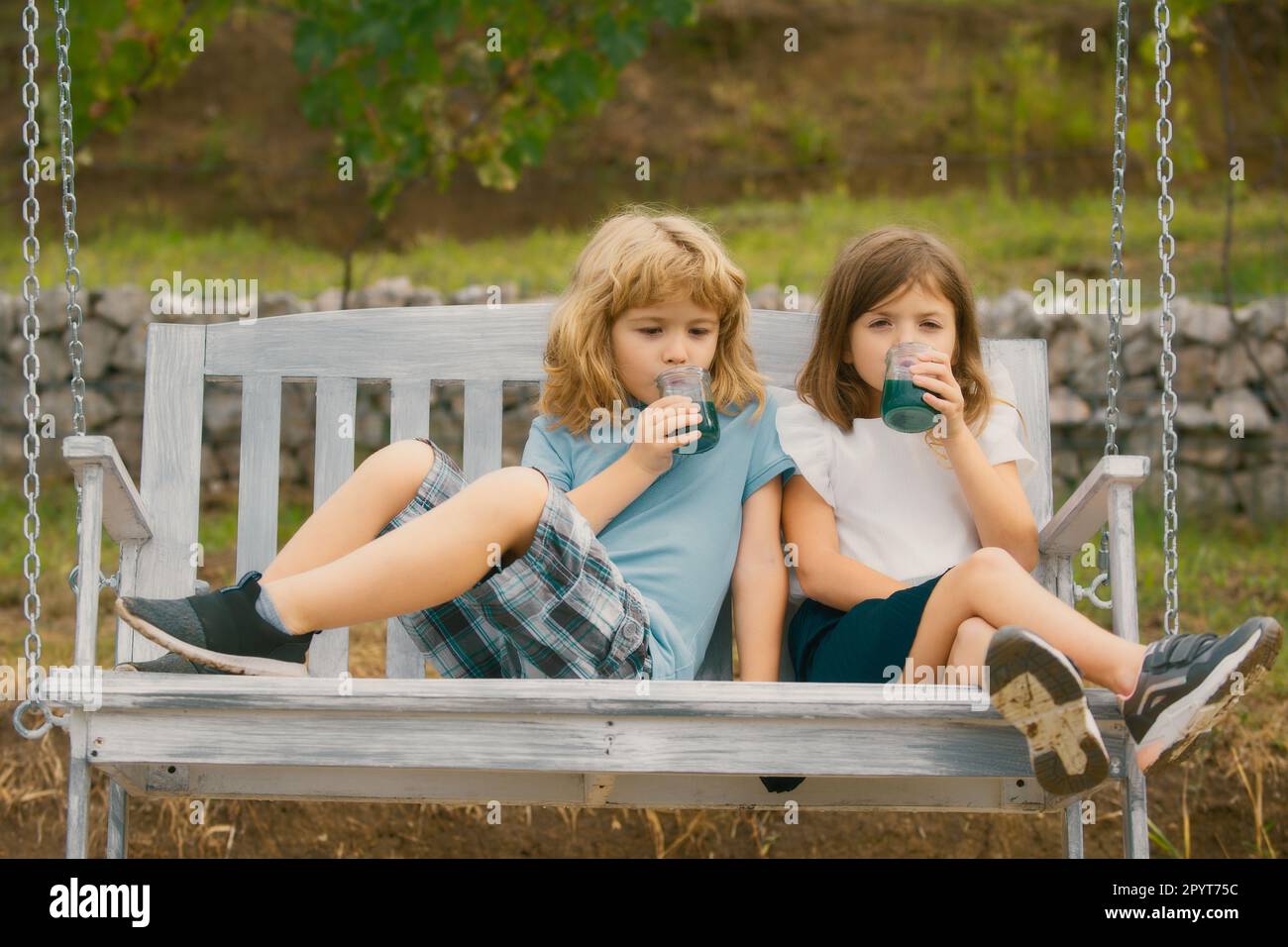 Happy brother and sister swinging on swing in summer park outdoors ...