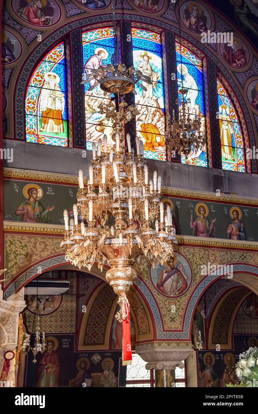 Interior of Orthodox church (side with stained glass window,the candelabrum and Byzantine hagiographies) in Greece Stock Photo