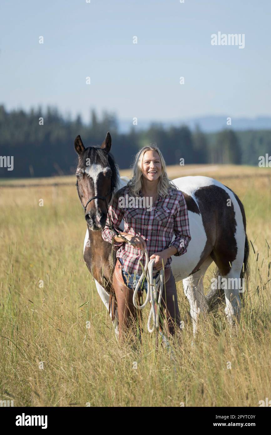 Mid adult woman standing with her horse on meadow and smiling, Bavaria, Germany Stock Photo
