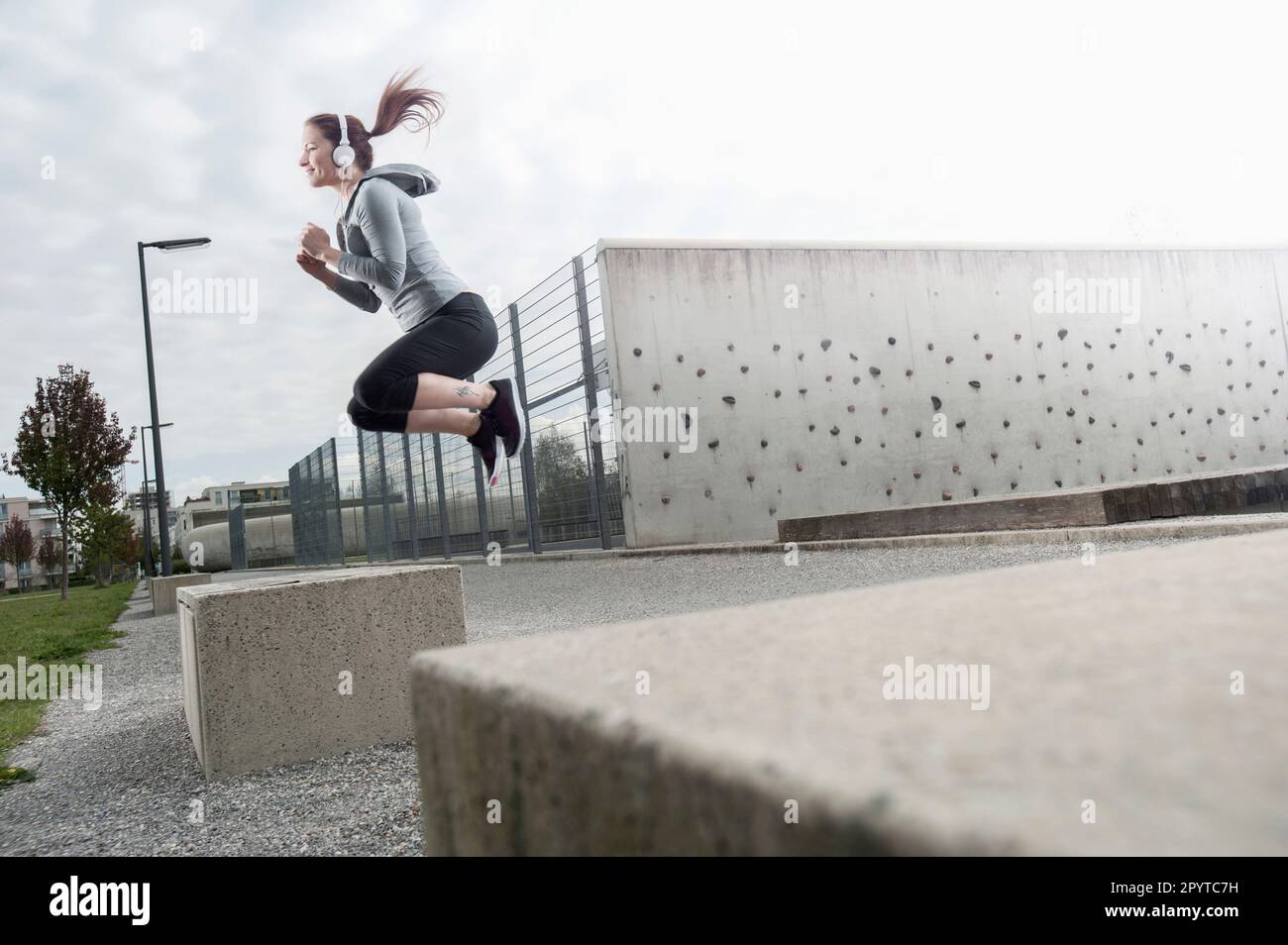 Young woman jumping on a concrete block and listening to music, Bavaria, Germany Stock Photo