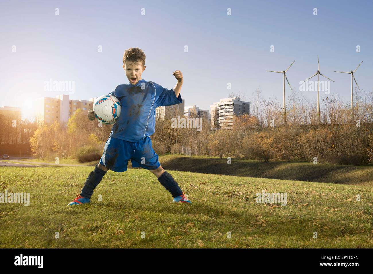 Dirty soccer player cheering on field and wind turbines with city in