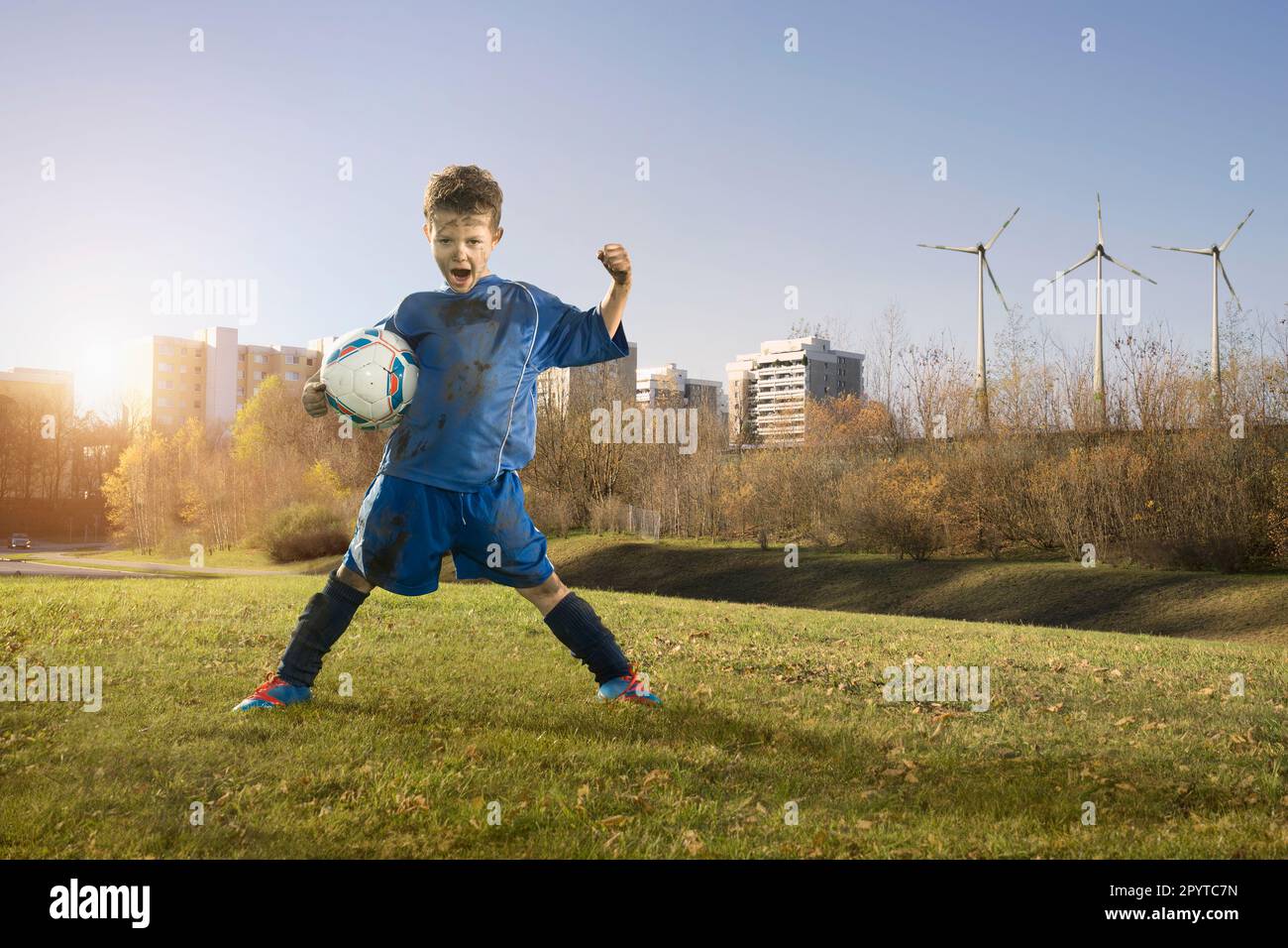 Dirty soccer player cheering on field and wind turbines with city in background, Bavaria, Germany Stock Photo