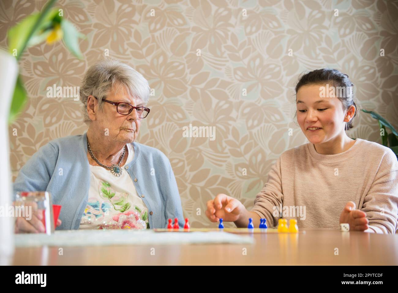 Girl playing board game with senior woman in rest home Stock Photo