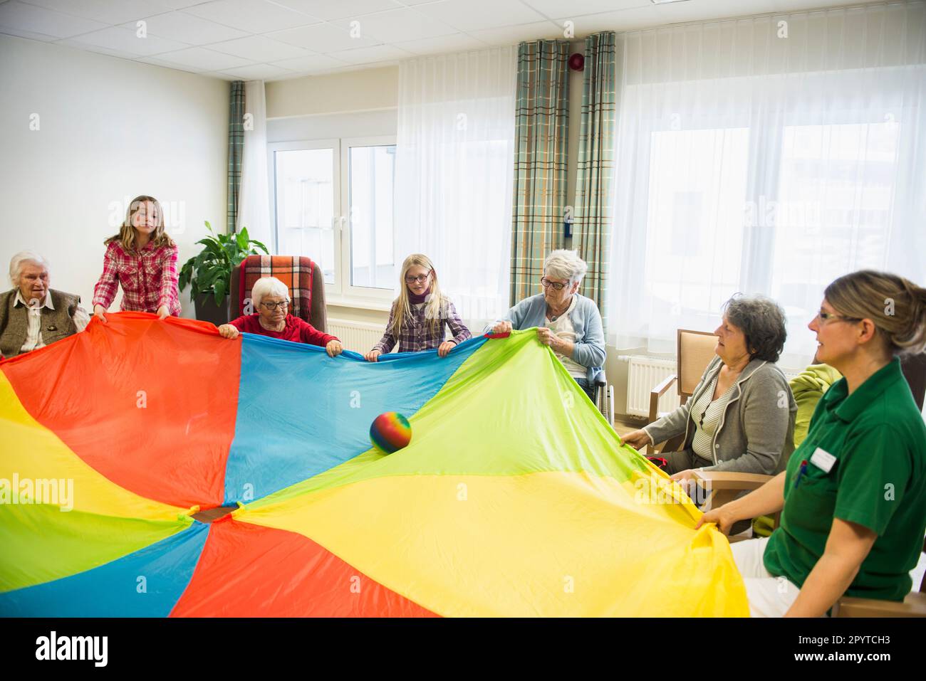 Nursing staff with girls and senior women doing sports exercise using parachute and ball in rest home Stock Photo