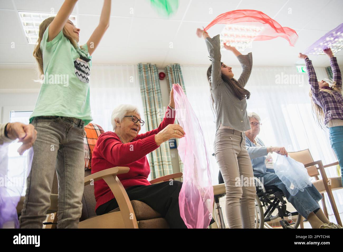 Girls and senior women doing gentle sports exercise using cloth in rest home Stock Photo