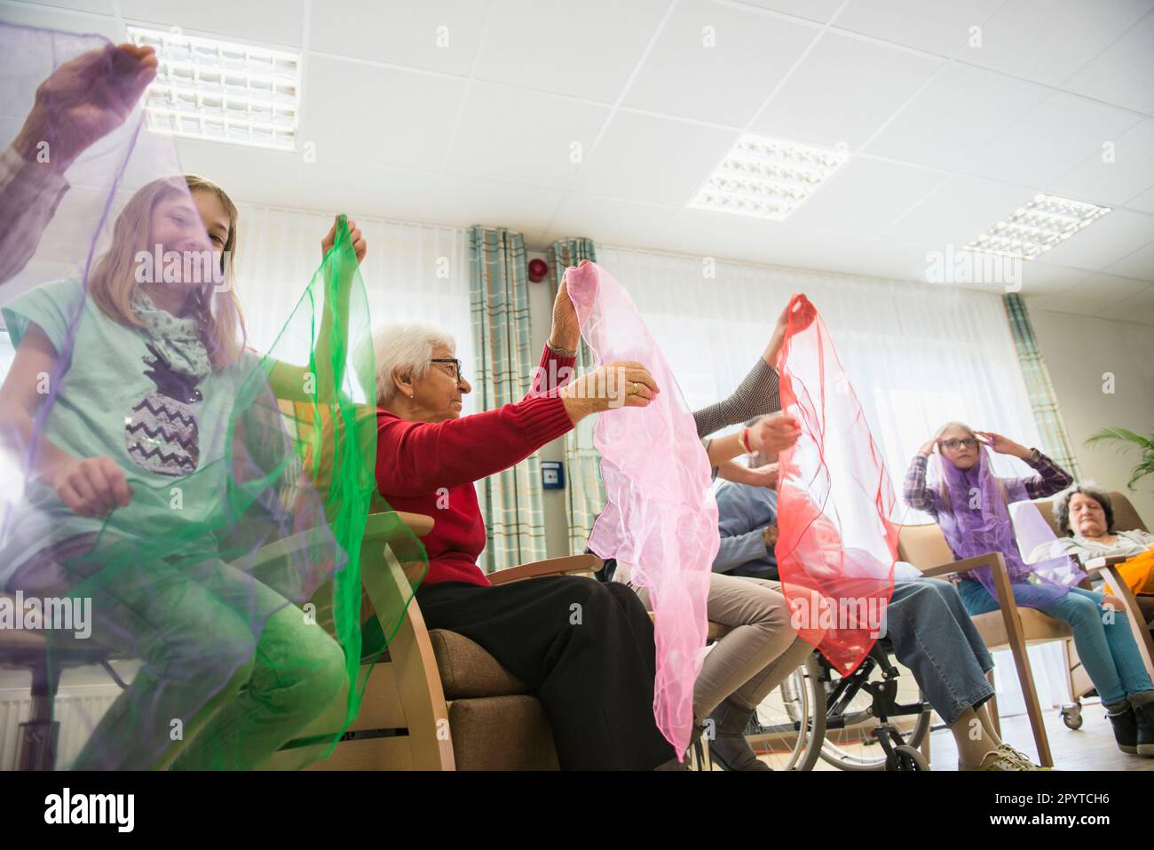 Girls and senior women doing gentle sports exercise with cloth in rest home Stock Photo