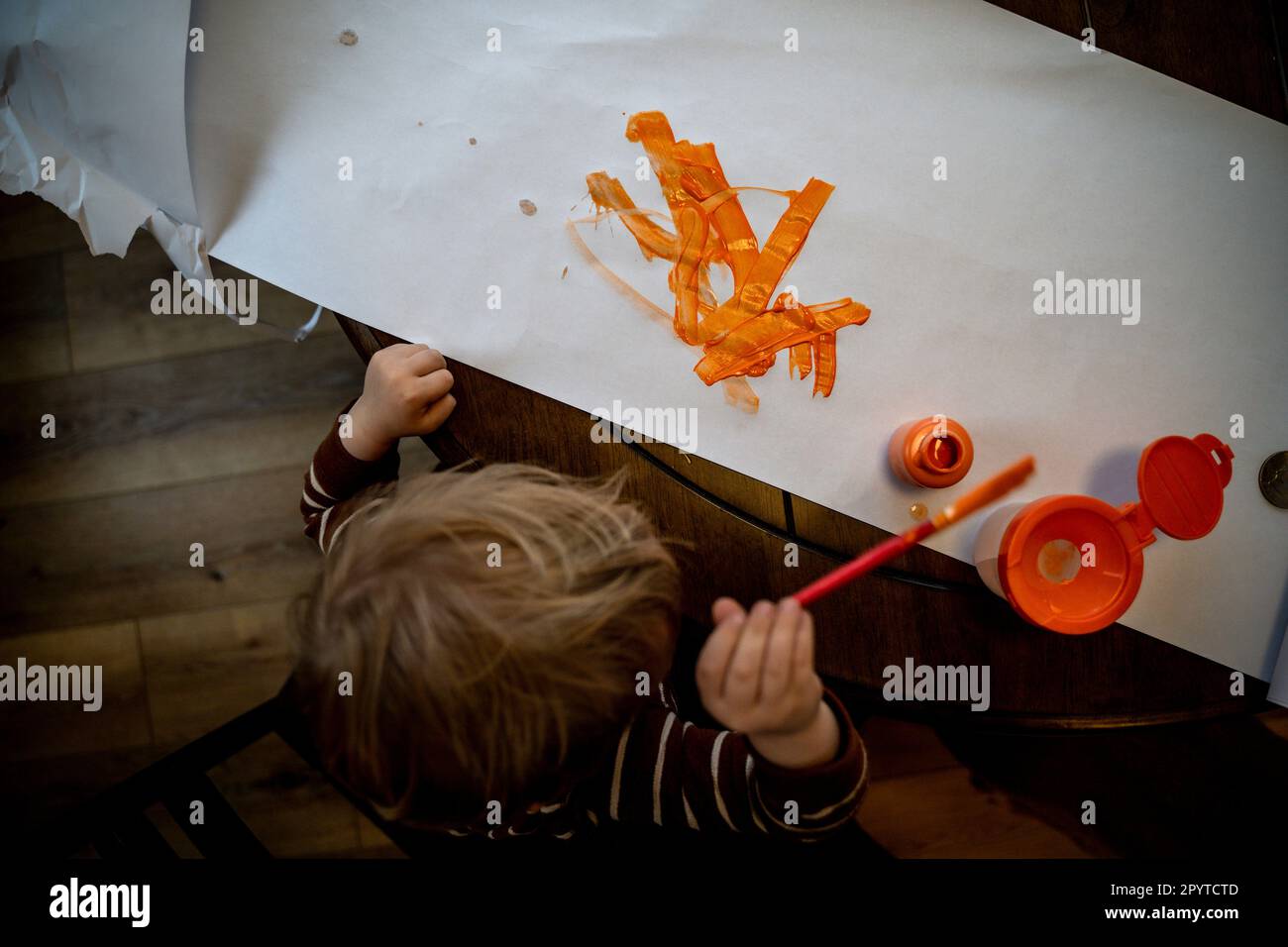 Blonde Toddler Boy Painting on White Paper with Orange Paint Stock Photo