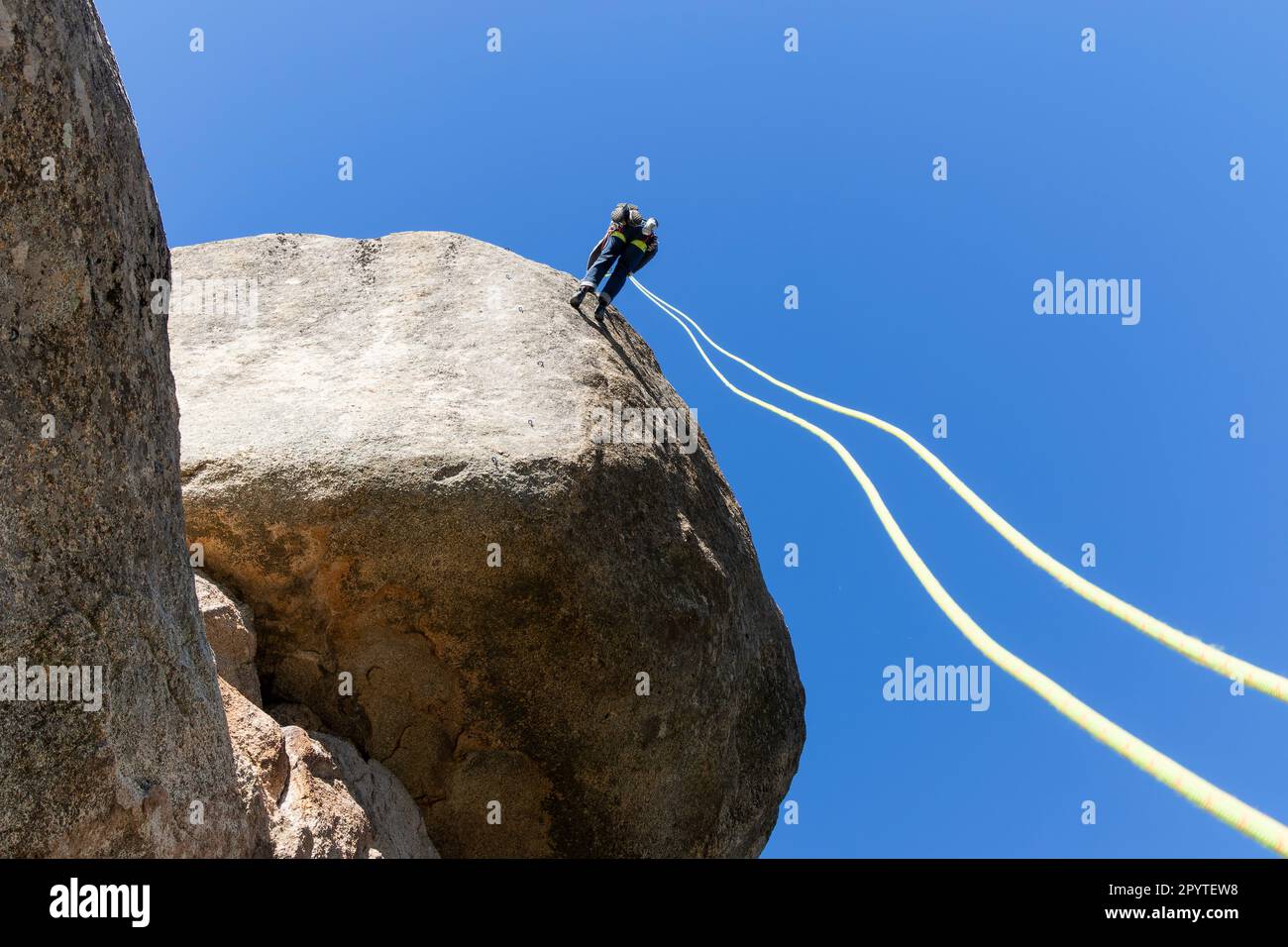 Young adult rock climber rappelling a granite wall in Torrelodones ...