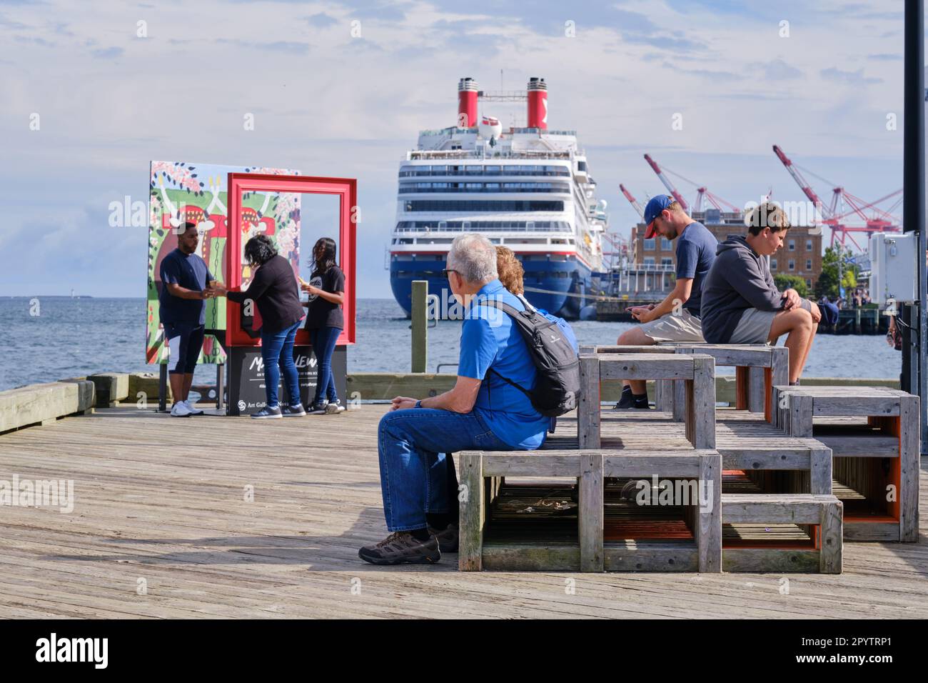 visitors sitting on bench on Halifax boardwalk with cruise ship in background Stock Photo