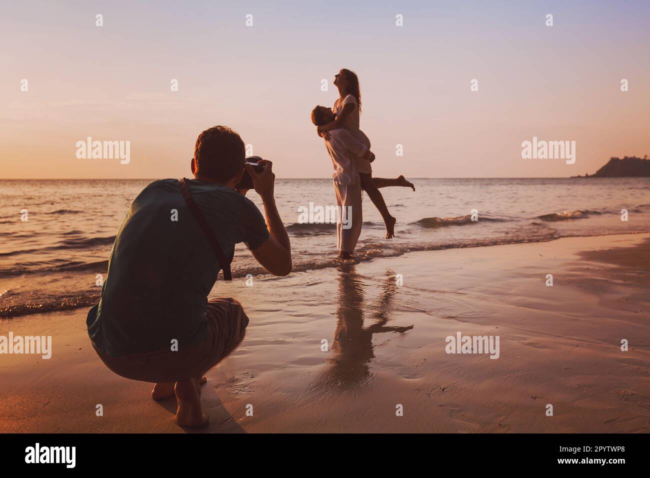 wedding portrait photographer taking photos of honeymoon couple on the beach at sunset, professional photography Stock Photo