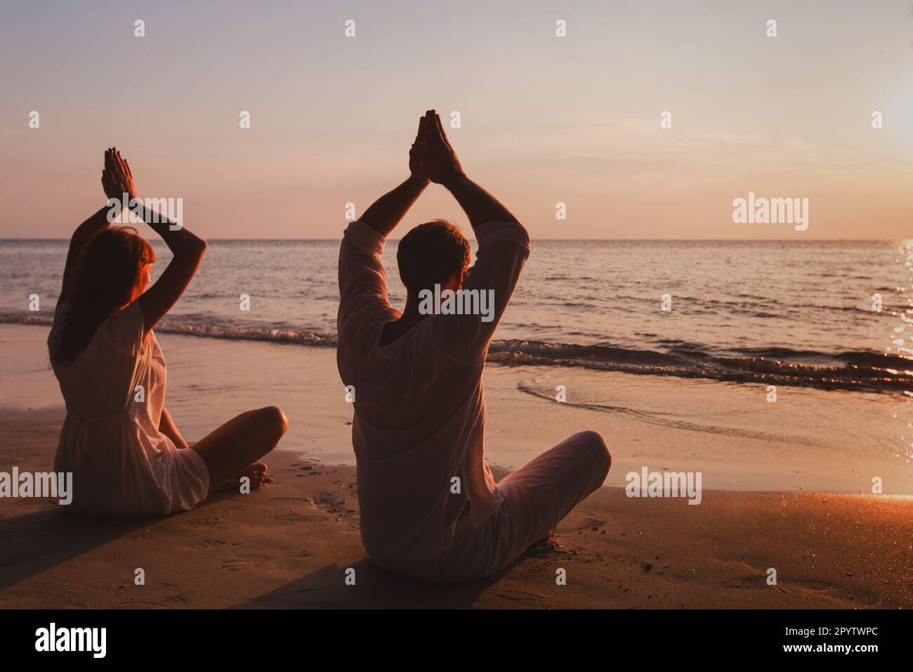 yoga on the beach, couple silhouettes practice meditation and breathing exercises, lotus position Stock Photo