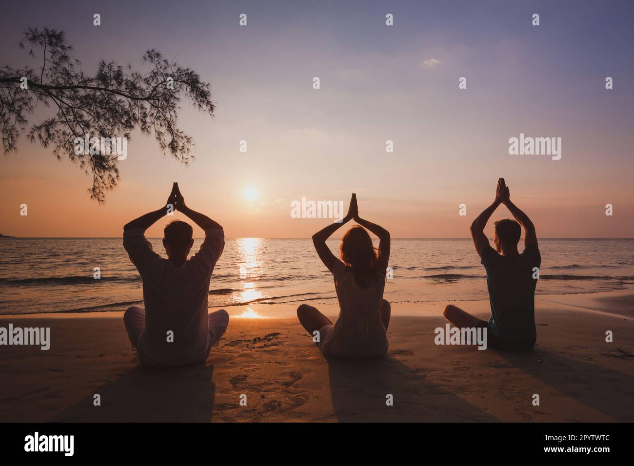 yoga group on the beach, silhouettes of people meditating in lotus position at sunset, meditation and breathing exercises Stock Photo