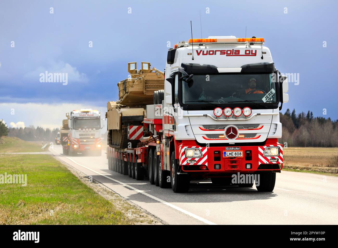 Mercedes-Benz truck hauls American M1 Abrams military tank on low loader semi trailer. Convoy of 3 oversize transports. Aura, Finland. April 28, 2023. Stock Photo