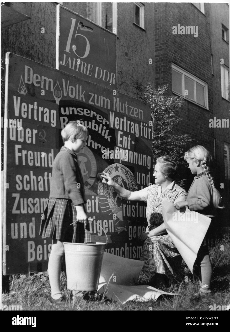 'Potsdam 1964 Preparations for Republic Day, a typical propaganda image, original caption: ''The Republic Day festive cleaning also begins in the residential areas. At Paul-Neumann-Strasse 29 in Babelsberg. Comrade Martin putting the finishing touches on a display stand. Marlis and Erwin were helpfully on hand.'' GDR. historical. Photo: MAZ/Manfred Haseloff, 1964 [automated translation]' Stock Photo