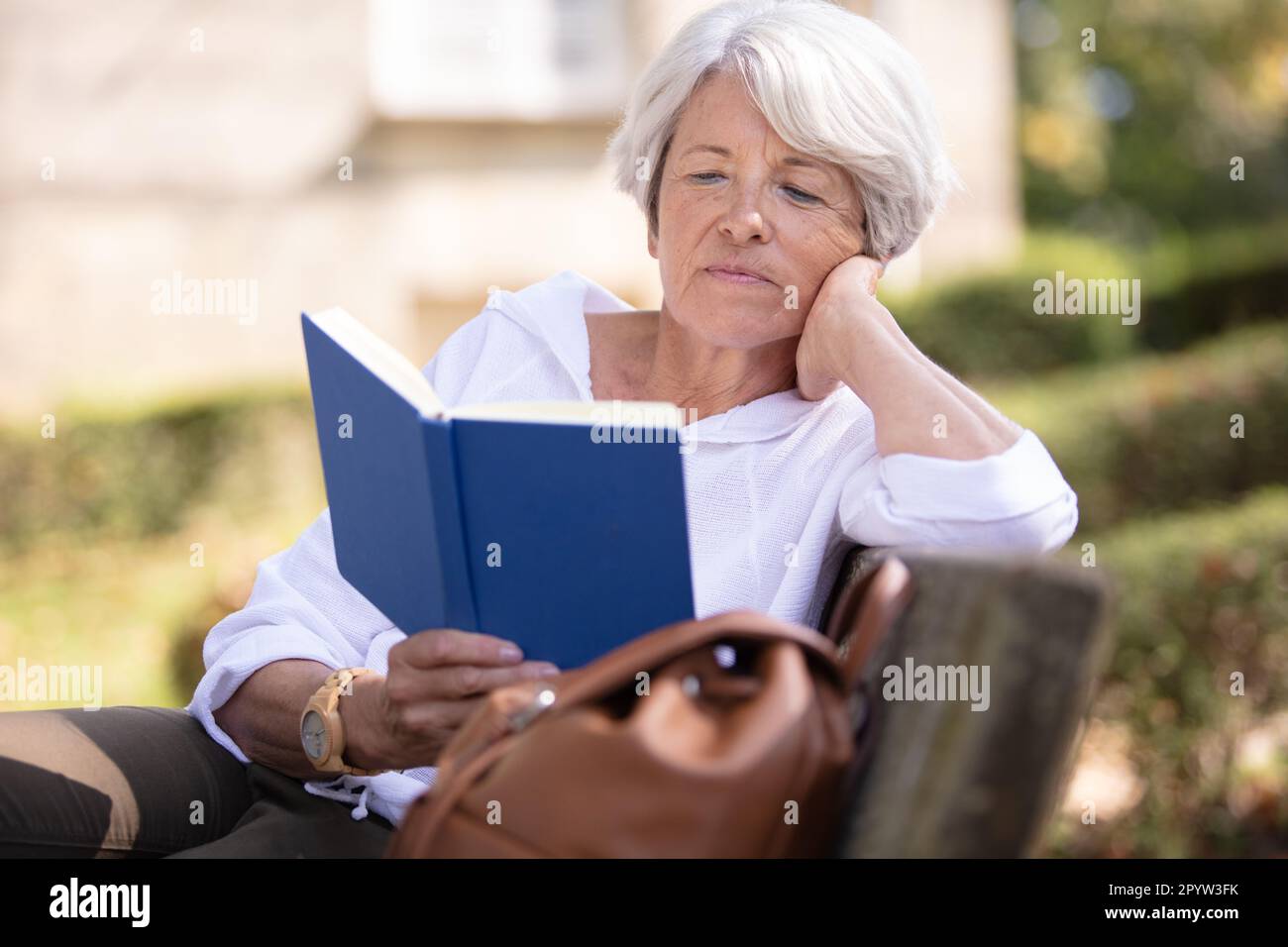 older woman sitting in park on bench reading a book Stock Photo - Alamy