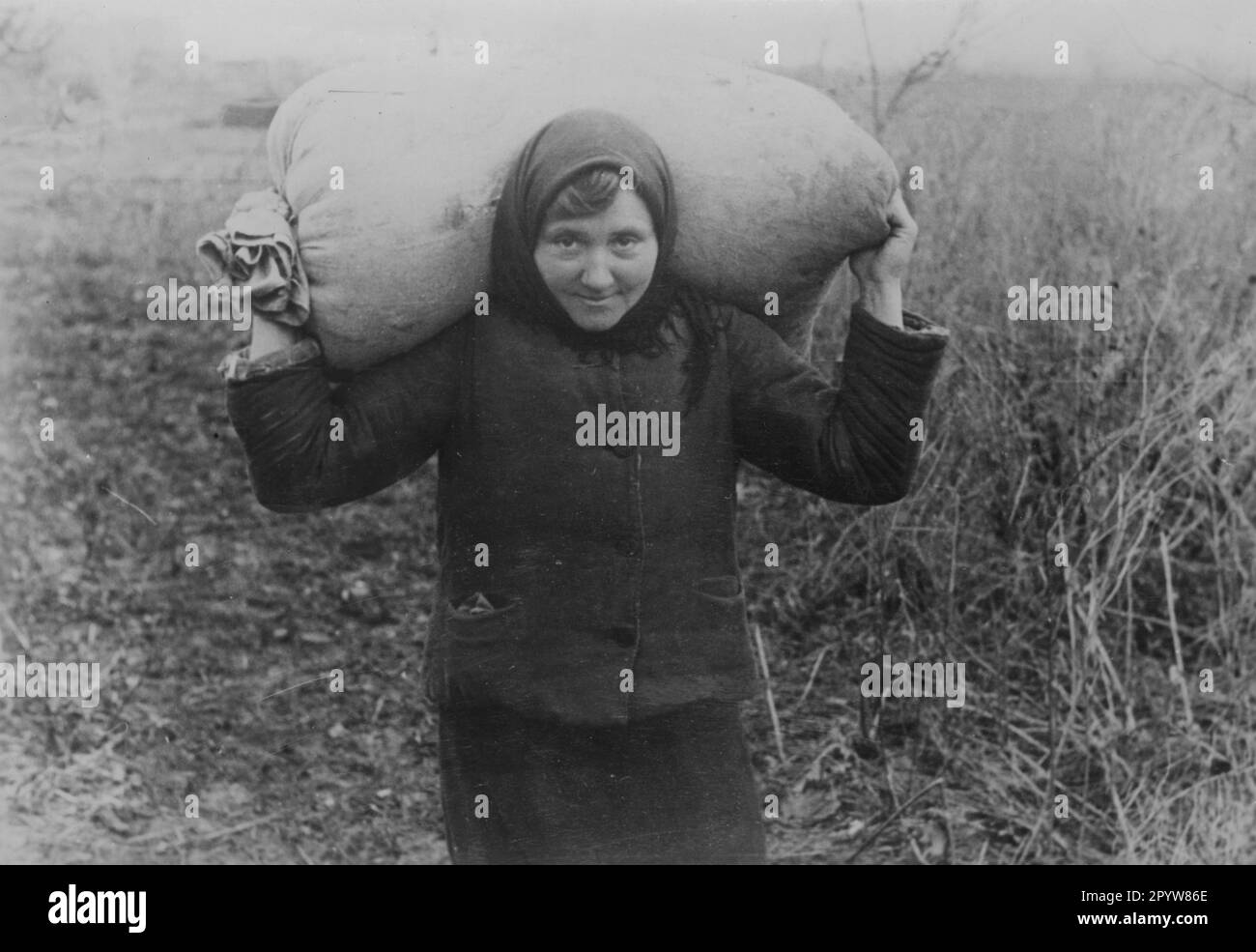 A woman in the German settlement Seraphimowka carries a sack of grain. Photo: Rebhahn. [automated translation] Stock Photo