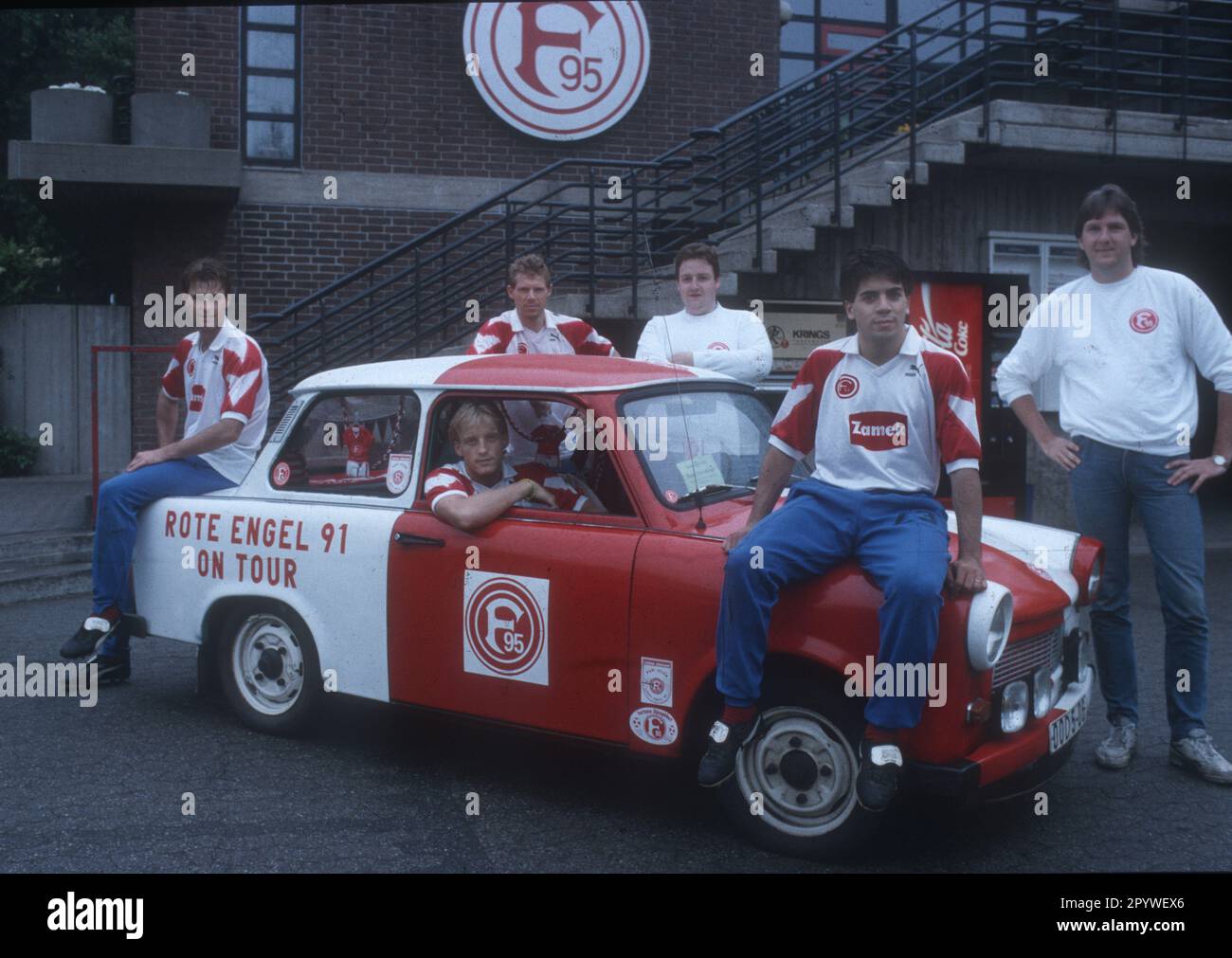 'Fortuna Düsseldorf season 1991/92. Players with a Trabbi of the fan club ''Rote Engel''. From left: Ralf Loose, Mike Büskens (in the car), Sven Demandt (in the back) and Marcello Carracedo (on the hood) together with two members of the fan club (white sweaters). 15.07.1991 (estimated). Only for journalistic use! Only for editorial use! [automated translation]' Stock Photo