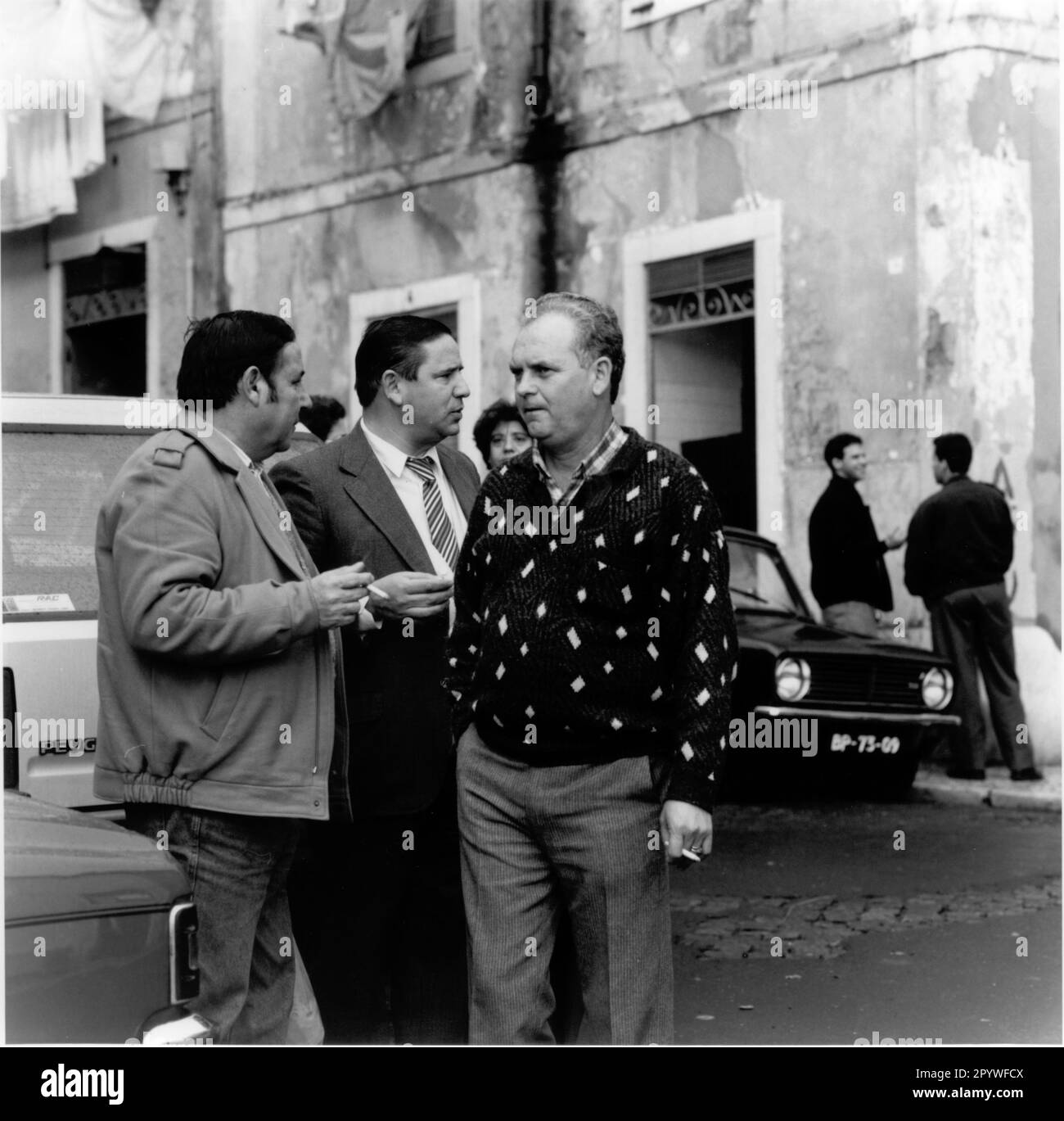 Portugal, Lisbon (Lisboa). Men with cigarettes in hand talking on the street, in front of a building. Street scene, black and white, 6x6 cm negative. Photo, 1992. Stock Photo
