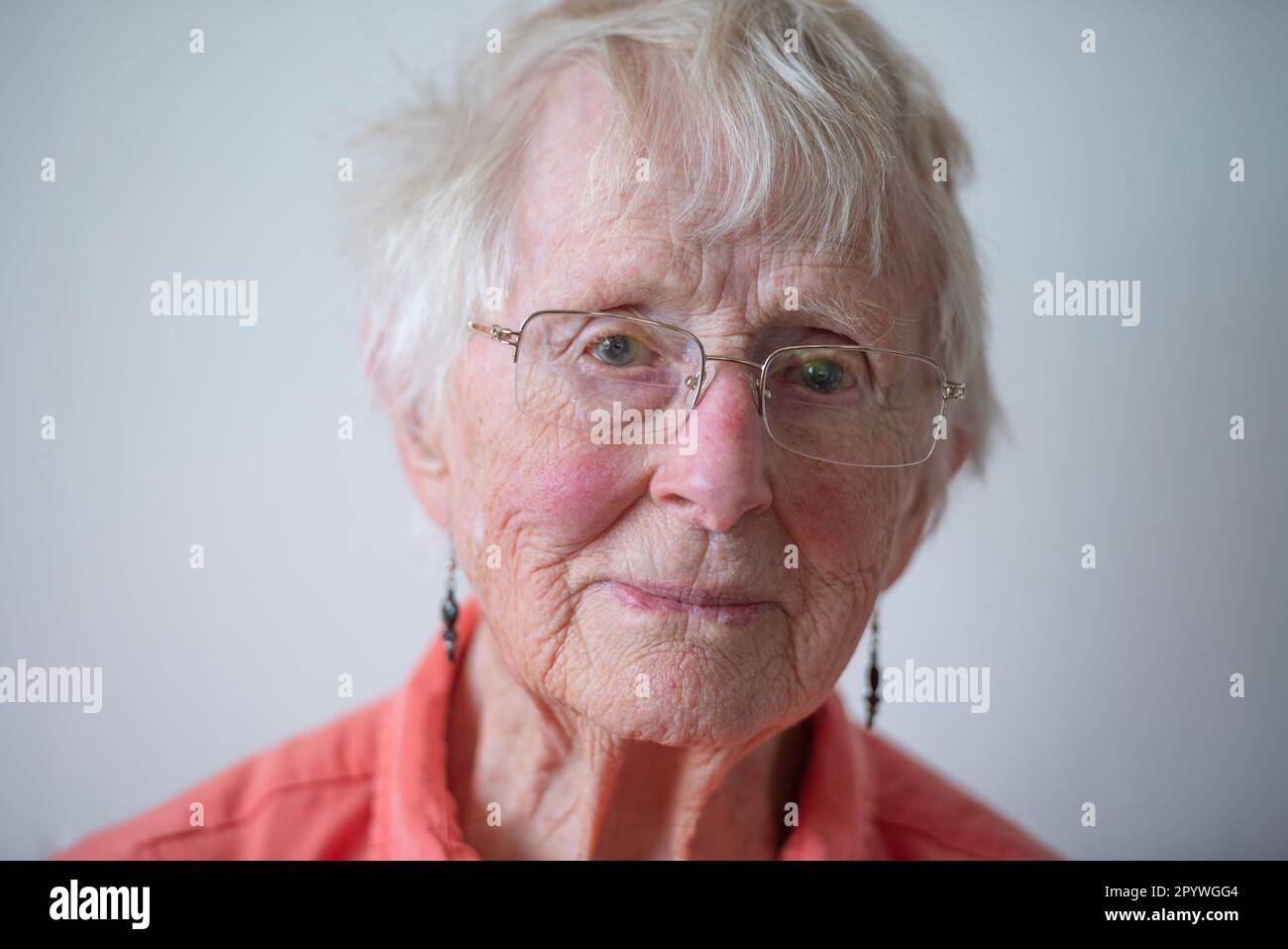 An elderly woman in her 90s, wearing an orange shirt lit with natural light from the side. Stock Photo