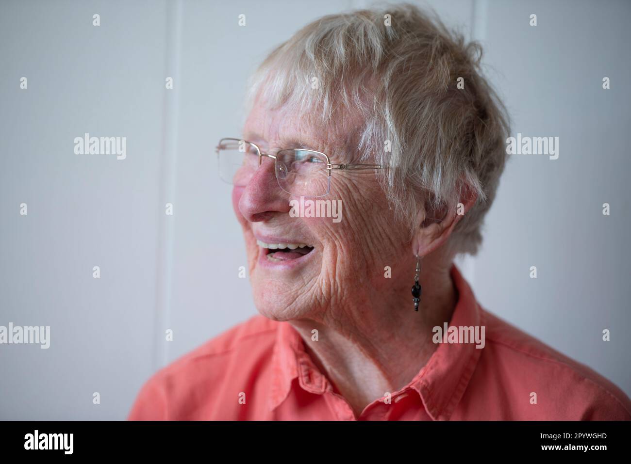 An elderly woman in her 90s, wearing an orange shirt lit with natural light from the side. Stock Photo