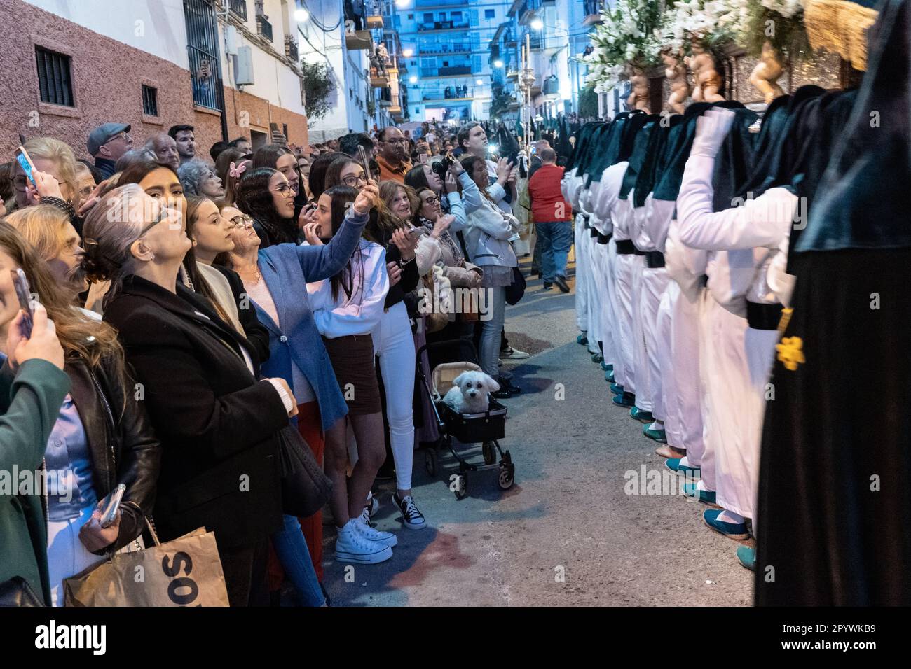 Bystanders watch as Nazarenos carry a massive platform with a statue of the Virgin Mary in a procession during Holy Week or Semana Santa, April 5, 2023 in Ronda, Spain. Ronda, first settled in the 6th century B.C. has been holding Holy Week processions for over 500-years. Stock Photo